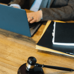 Gavel resting on the desk. A person in the background on a laptop