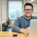 Man at his laptop smiling: Employers' Guide to the New Flexible Working Law 2024